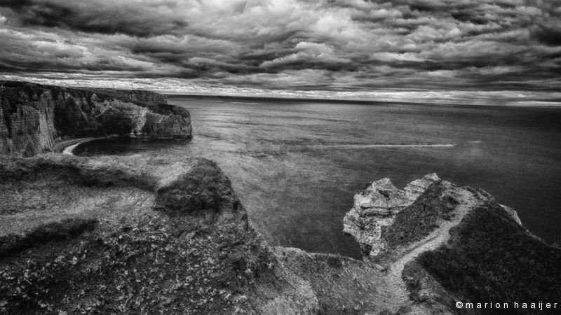 Zwart-witfoto van de kliffen bij Étretat onder een bewolkte hemel