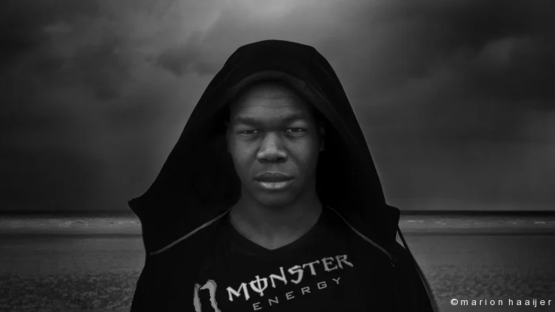 Zwart-witportret van een man met een capuchon aan zee